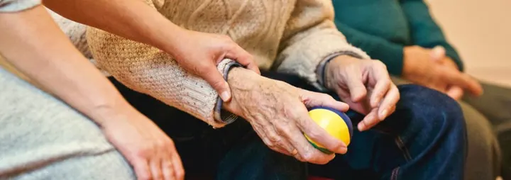 Close view of a carer guiding an older person through a hand exercise with a soft ball.