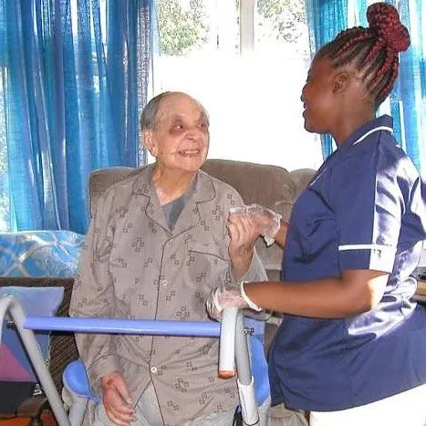 A Muzaana carer steadying an older woman at her walking frame, both of them smiling.