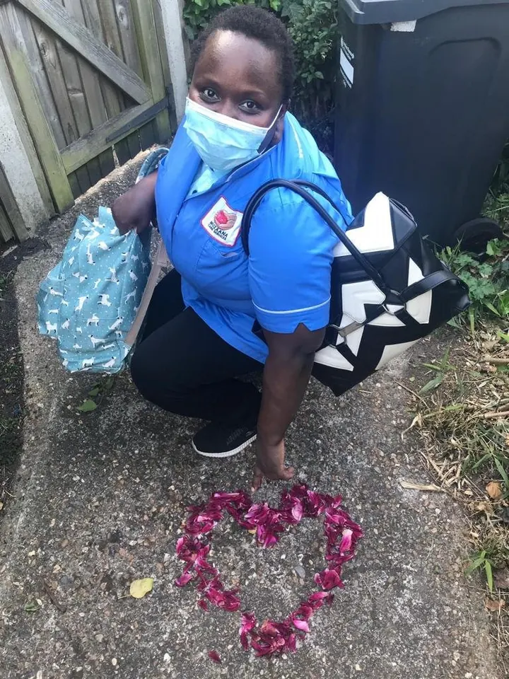 A Muzaana carer in a face mask crouching beside a heart laid out in pink petals on a doorstep.