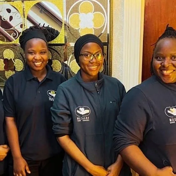 Muzaana carers in branded uniform standing together indoors, smiling.