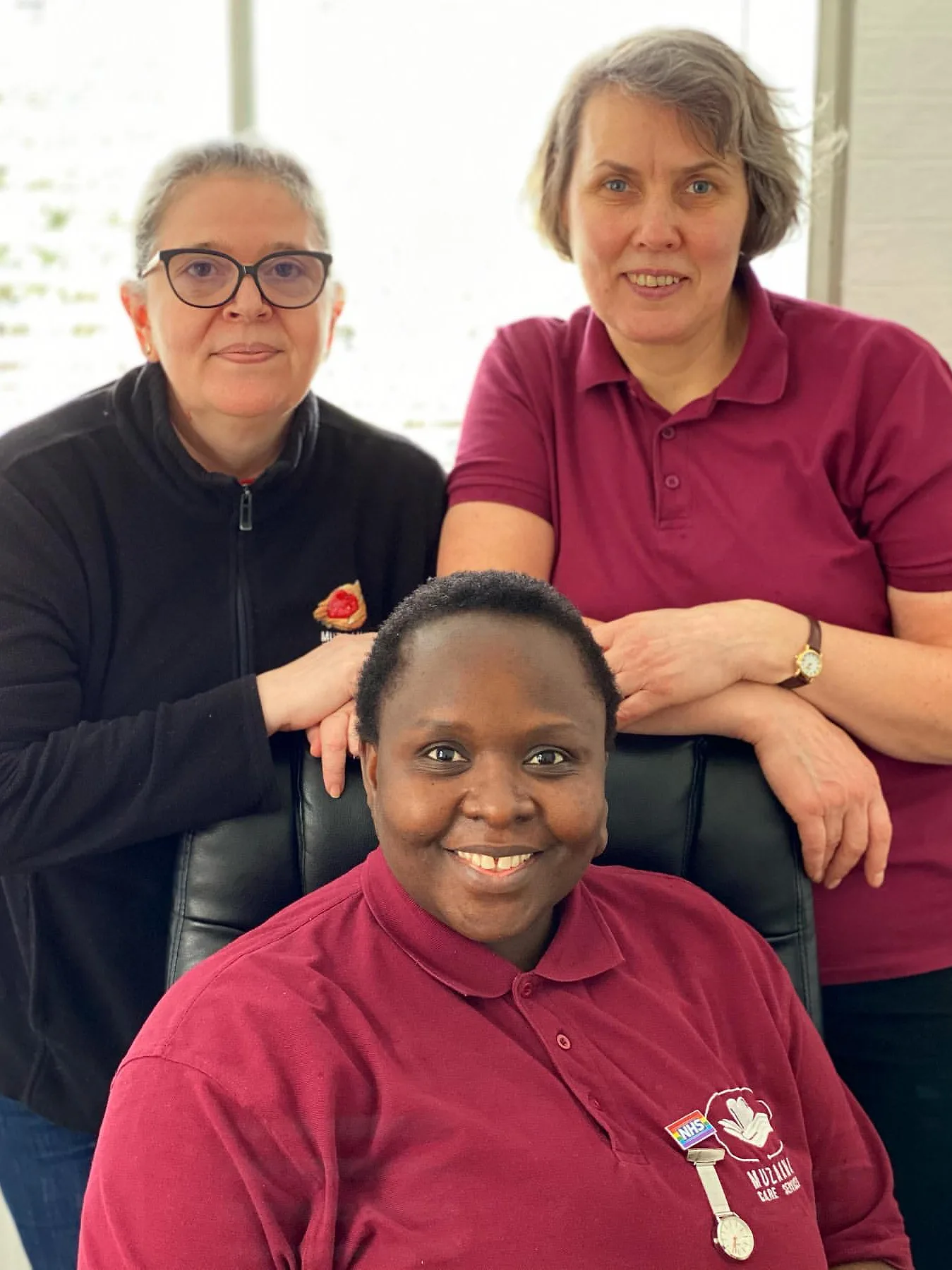 Three Muzaana staff in branded uniform indoors, one seated and two standing behind, all looking to camera.