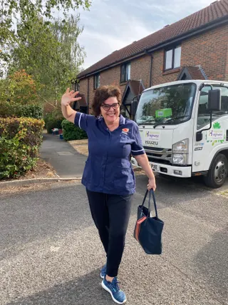A Muzaana carer in navy uniform, bag in hand, waving on a residential street.