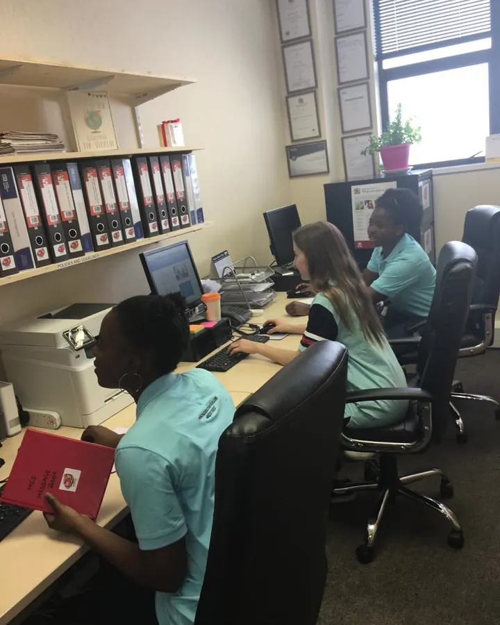 A Muzaana carer updating care records at a computer, a client folder open beside her.